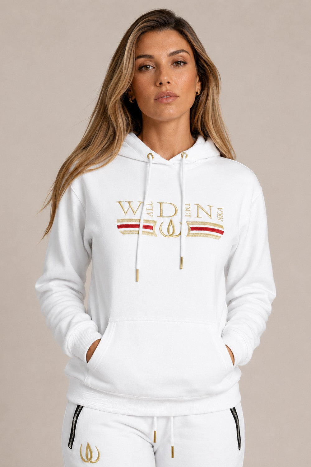 Hvid Deluxe Hoodie med guldbroderi og rød stribe over brystet, båret til hvide Deluxe Joggers med guldlogo.