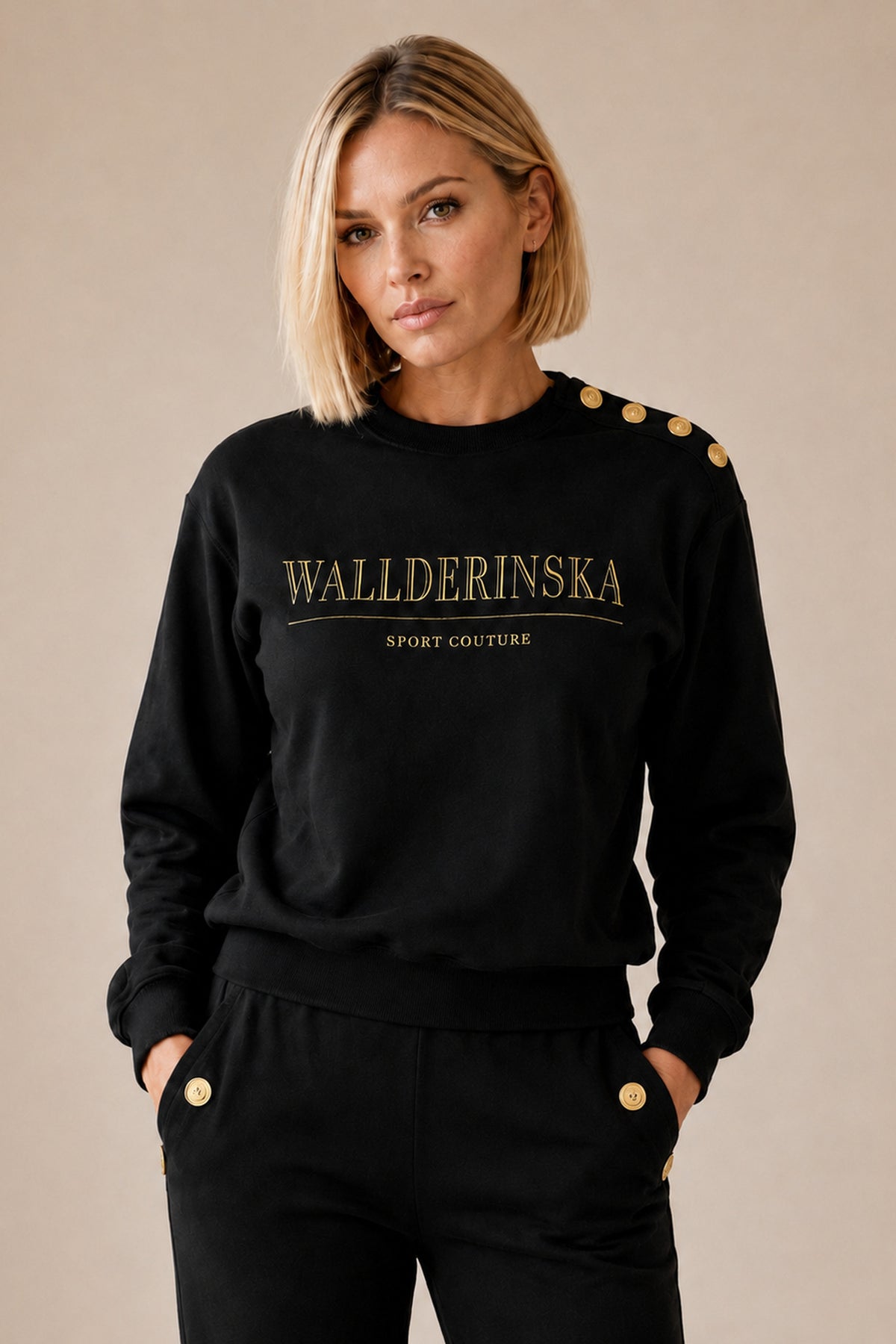Edge Gold Button-setet i svart framifrån, med händerna i byxfickorna där guldknapparna sitter.