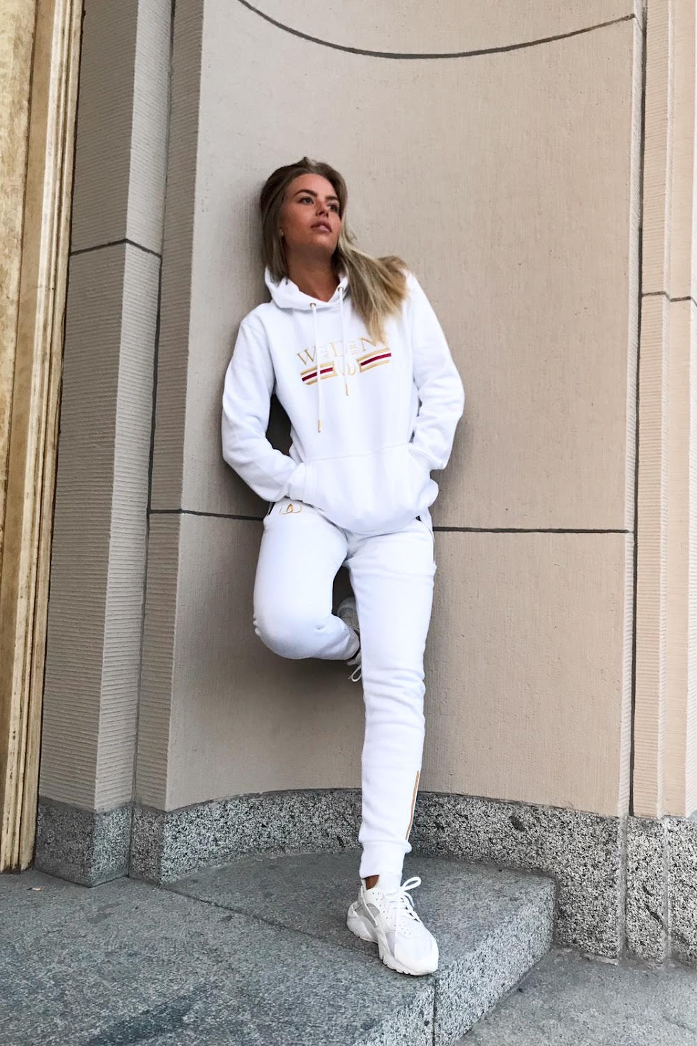 Op ad husmuren står modellen i hvid hættetrøje og hvide joggers, til hvide sneakers.