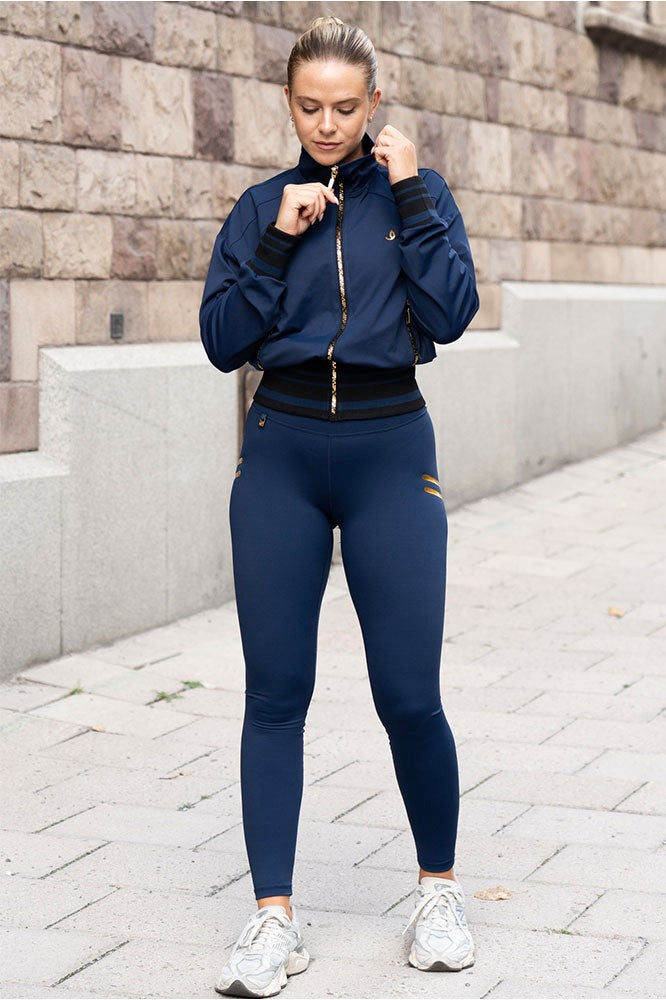 Modellen bærer de marineblå tights og en jakke i samme tone med guldfarvet lynlås, i byen.