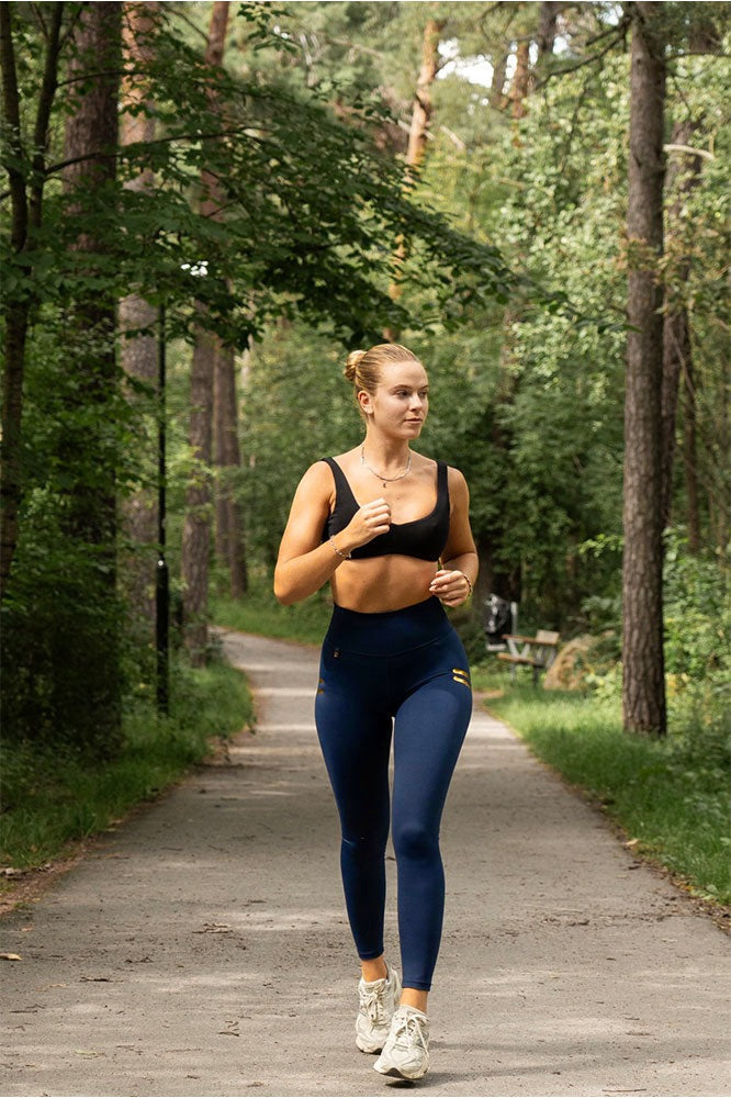 Løb på en skovvej i marineblå tights med guldstriber og sort sports-bh.