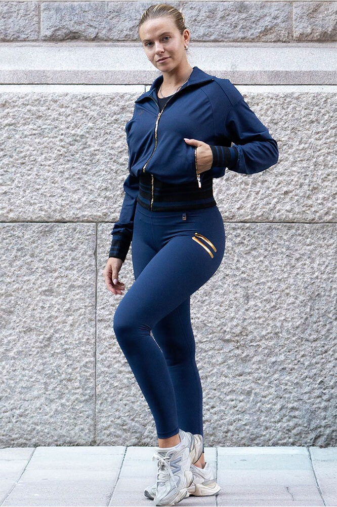 Mod granitvæggen ses de marineblå tights med en åben jakke med guldfarvede lynlåse.