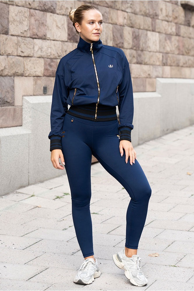 Udendørs i marineblå jakke med guldfarvede lynlåse, marineblå tights og hvide sneakers.